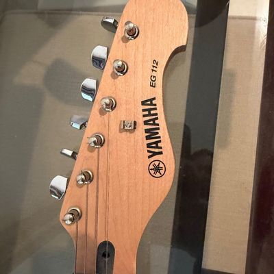 Sale Photo Thumbnail #289: Headstock of a Yamaha EG 112 electric guitar, showing the natural wood finish, tuning pegs, and brand logo.