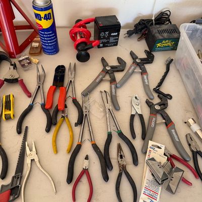 Assorted hand tools including various pliers, wire cutters, and RoboGrip wrenches, displayed alongside a Battery Tender Plus charger,...
