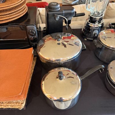 Sale Photo Thumbnail #270: Assorted kitchenware including stainless steel pots with lids, an Osterizer blender, a black espresso machine, a toaster oven, woven chargers, and orange napkins.