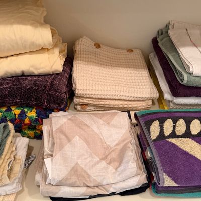 Sale Photo Thumbnail #166: Assorted household linens and towels, including waffle-weave hand towels, patterned bath towels, and folded sheets, arranged on a shelf.