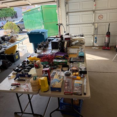 Assorted garage and household items displayed on folding tables, including hand tools, painting supplies, extension cords, and small...