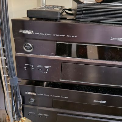Yamaha Natural Sound AV Receiver RX-V1000 and RX-V1200 units stacked on a wire shelf, showing some surface dust.