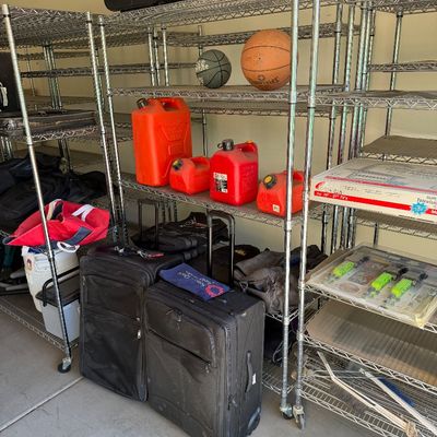 Assorted garage items including chrome wire shelving units, black rolling suitcases, red plastic gas cans, and basketballs.