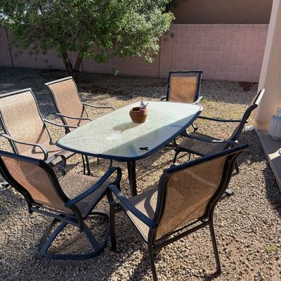 Sale Photo Thumbnail #243: Outdoor patio dining set featuring an oval glass-top table with a dark metal frame and six matching mesh-backed chairs, including two swivel rockers.
