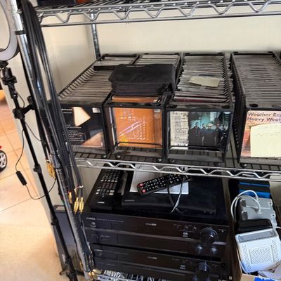 Wire shelving unit holding a collection of CDs in storage racks, home audio components including a Yamaha receiver, and various...