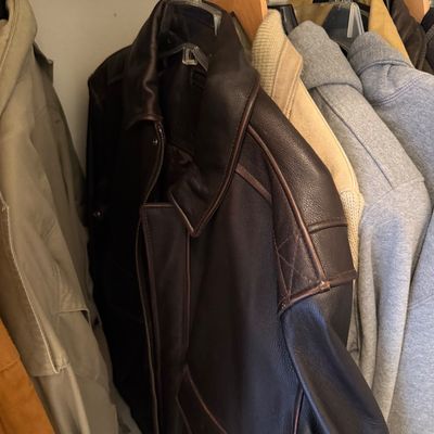 Sale Photo Thumbnail #174: Assorted men's outerwear hanging in a closet, featuring a dark brown leather bomber jacket alongside casual jackets and hoodies.