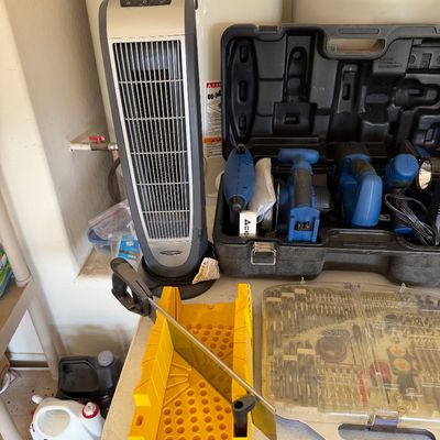 Lasko ceramic tower heater, a yellow plastic miter box with hand saw, a large drill bit set, and a black hard case containing various...