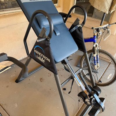 Sale Photo Thumbnail #226: Ironman Memory Foam inversion table with a blue padded backrest and sturdy steel frame, shown alongside a blue mountain bike.