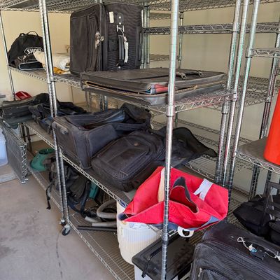 Assorted luggage, duffel bags, and briefcases displayed on heavy-duty wire shelving units.