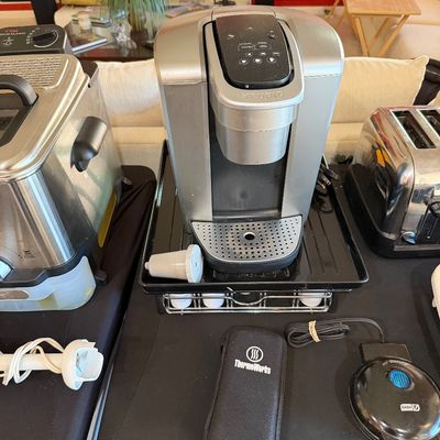 Sale Photo Thumbnail #263: Keurig single-serve coffee maker in silver and black, displayed alongside other small kitchen appliances including a deep fryer, toaster, and hand blender.