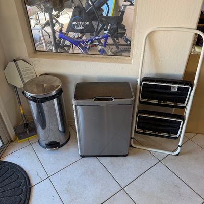 Sale Photo Thumbnail #252: Two stainless steel trash cans, including a round step-on model and a rectangular sensor model, shown alongside a white metal two-step folding ladder.