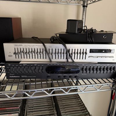 Vintage Realistic Twelve Band Stereo Frequency Equalizer and an AudioSource EQ 100 Graphic Equalizer and Spectrum Analyzer, stacked on a...