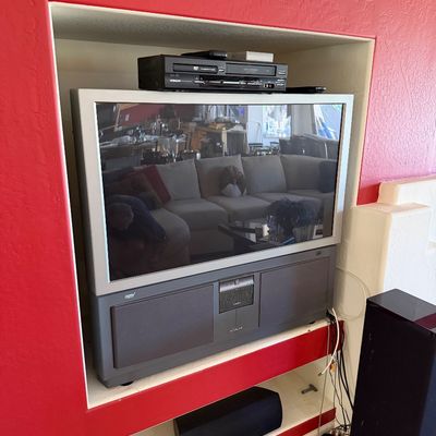 Sale Photo Thumbnail #290: Vintage Hitachi rear-projection television with a silver bezel and integrated lower speaker cabinet, shown with a VCR/DVD player on top.