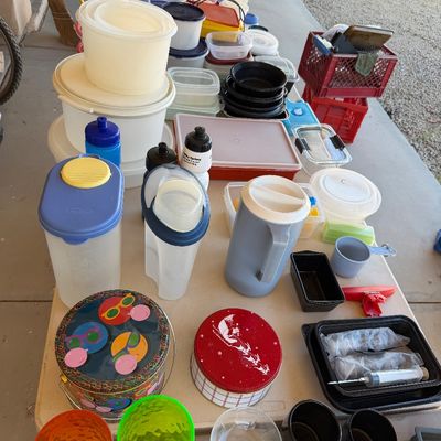 Sale Photo Thumbnail #232: Assorted household items, including plastic food storage containers, water pitchers, decorative tins, and colorful glassware, arranged on a folding table.
