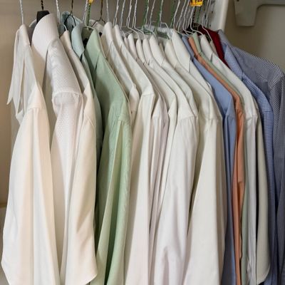 Sale Photo Thumbnail #129: Collection of men's long-sleeve dress shirts hanging in a closet, featuring various solid colors including white, light green, blue, and peach.