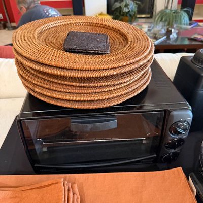 Sale Photo Thumbnail #267: Black Oster toaster oven topped with a stack of woven rattan charger plates, shown alongside orange fabric placemats.