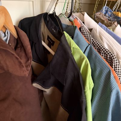 Sale Photo Thumbnail #156: Assortment of men's vintage and contemporary shirts, including a brown suede jacket and a black and tan color-blocked silk shirt, hanging on a closet rod.