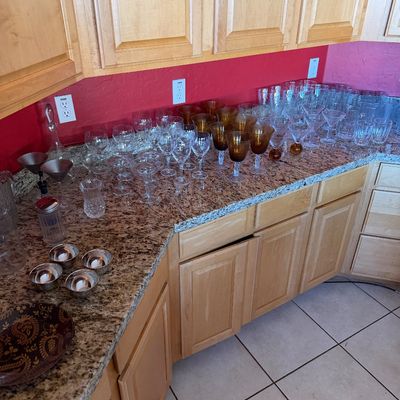 Large collection of assorted glassware, including amber-colored goblets, clear wine glasses, martini glasses, and small silver-toned...