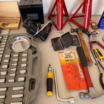 Assorted hand tools and garage equipment, including a socket set, hammers, screwdrivers, drill bits, and a pair of red jack stands.