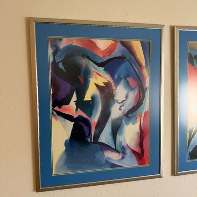 Sale Photo Thumbnail #315: Framed abstract watercolor print featuring fluid shapes in blue, red, and yellow, presented in a silver-toned frame with a blue mat.