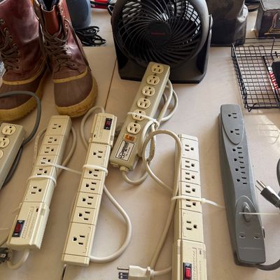 Sale Photo Thumbnail #110: Assorted power strips, a small Honeywell desk fan, and a pair of Sorel-style winter boots displayed on a table.