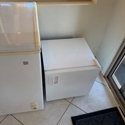 Sale Photo Thumbnail #251: Compact white mini-fridge or freezer sitting on a tiled floor next to a larger chest freezer.