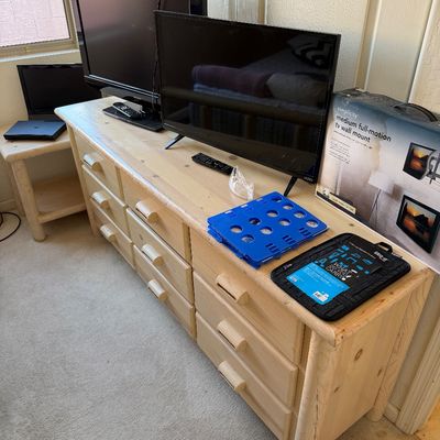 Sale Photo Thumbnail #190: Light pine log-style nine-drawer dresser, shown with two flat-screen televisions, a boxed TV wall mount, and other small electronics.