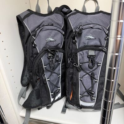 Sale Photo Thumbnail #127: Pair of High Sierra hydration backpacks in gray and black, featuring multiple zippered compartments and bungee cord storage.