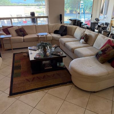 Large contemporary U-shaped sectional sofa in beige fabric, featuring a rounded chaise end and styled with various accent pillows.