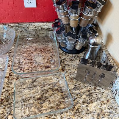 Sale Photo Thumbnail #216: Assorted kitchenware including two clear glass baking dishes, a rotating chrome spice rack with jars, a stainless steel pepper mill, and a metal napkin holder with utensil cutouts.
