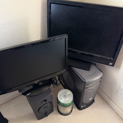 Vintage Dell desktop computer tower, a Vizio flat-screen monitor, a ViewSonic monitor, a speaker, and a spindle of blank CDs.