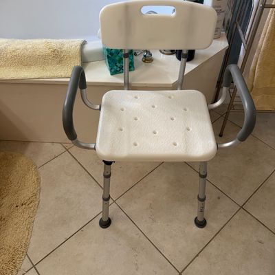 Sale Photo Thumbnail #137: Adjustable medical shower chair with a white plastic seat and backrest, padded armrests, and non-slip rubber feet.