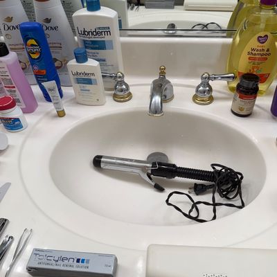 Sale Photo Thumbnail #133: Assorted personal care items, including Lubriderm lotion, Dove body wash, and a curling iron, arranged around a bathroom sink.