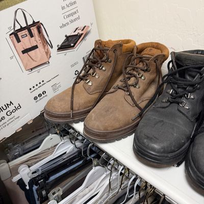 Sale Photo Thumbnail #128: Two pairs of lace-up ankle boots, one in brown nubuck leather and one in black, showing moderate wear and stored on a closet shelf.