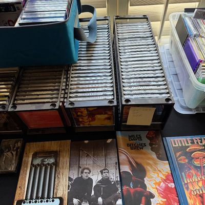 Collection of music CDs in storage racks and cases, alongside box sets including Miles Davis's "Bitches Brew" and Simon...