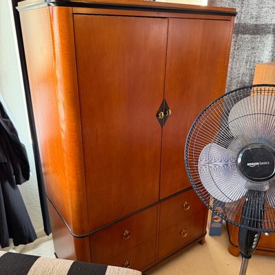 Sale Photo Thumbnail #150: Art Deco style wooden armoire featuring a warm cherry finish, rounded corners, two upper cabinet doors, and four lower drawers with brass ring pulls.