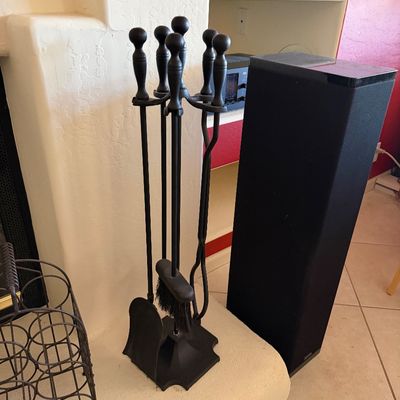 Black wrought iron fireplace tool set with stand, alongside a tall black floor-standing speaker.