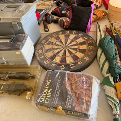 Assorted garage and outdoor items including a Sportcraft dartboard, a box of hickory smoking chips, plastic toolboxes, umbrellas, and...