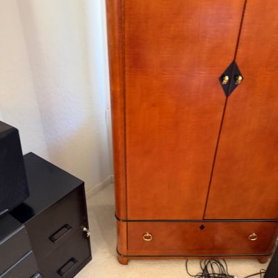 Sale Photo Thumbnail #146: Art Deco style cherry wood armoire featuring a two-door cabinet with diamond-shaped black pulls and a bottom drawer with brass ring pulls.