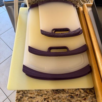 Sale Photo Thumbnail #222: Set of three nesting plastic cutting boards with purple handles, stacked on top of a larger yellow cutting board.