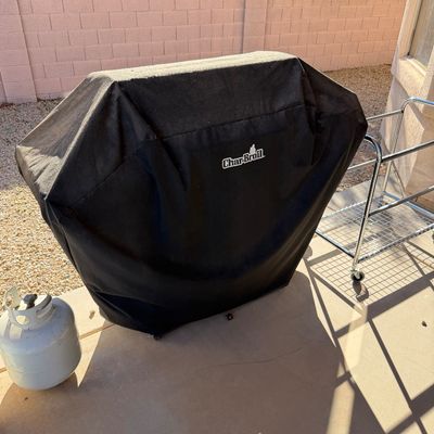 Sale Photo Thumbnail #241: Char-Broil outdoor grill with a black protective cover, shown alongside a propane tank and a chrome rolling cart.