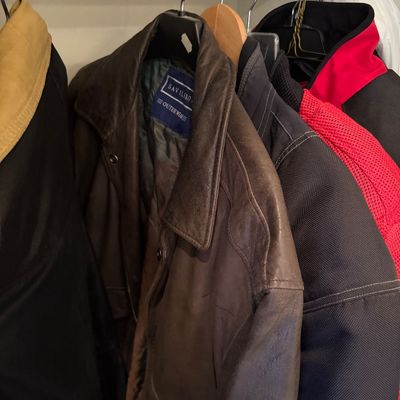 Sale Photo Thumbnail #183: Savilero Outerwear brown leather jacket hanging on a closet rod alongside other jackets, including a Firstgear motorcycle jacket.