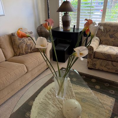 Sale Photo Thumbnail #317: Postmodern triangular glass-top coffee table with a textured stone base, styled with a clear glass vase of calla lilies and a stone sphere.