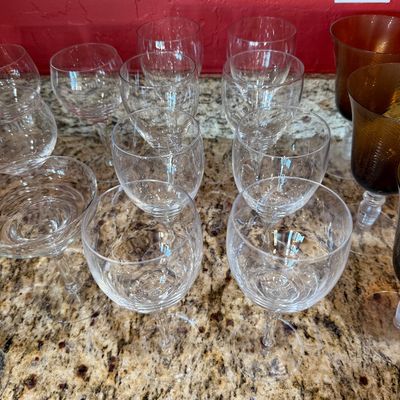 Sale Photo Thumbnail #213: Collection of clear crystal wine glasses and stemware, displayed alongside amber-colored goblets on a granite countertop.