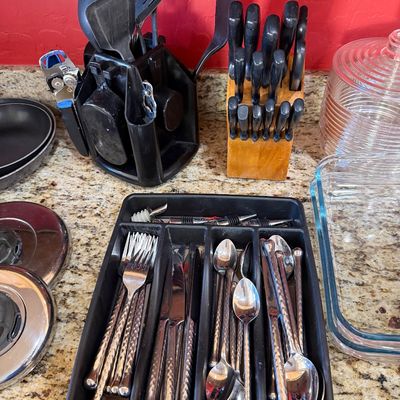 Sale Photo Thumbnail #223: Assorted kitchenware including a flatware set with textured handles in a black organizer, a wooden knife block set, a rotating utensil caddy, and glass baking dishes.