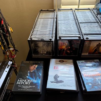 A collection of DVDs and CDs, including titles like Minority Report, Fargo, and Ronin, organized in black plastic storage racks.