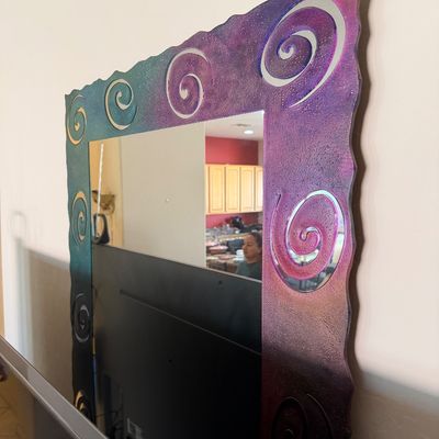 Sale Photo Thumbnail #271: Contemporary wall mirror featuring a textured, wavy-edged frame with a metallic gradient finish in purple, teal, and gold, accented by spiral cutouts.