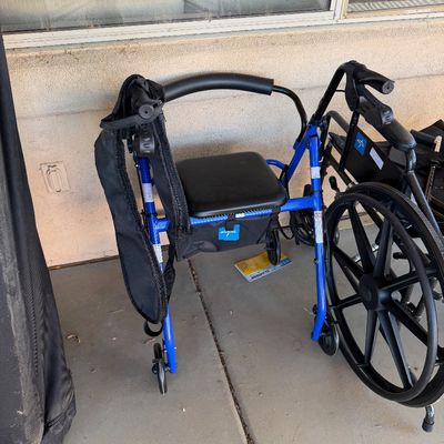 Sale Photo Thumbnail #254: Medline blue four-wheel rollator walker with a padded seat, backrest, and under-seat storage pouch, shown alongside a black wheelchair.