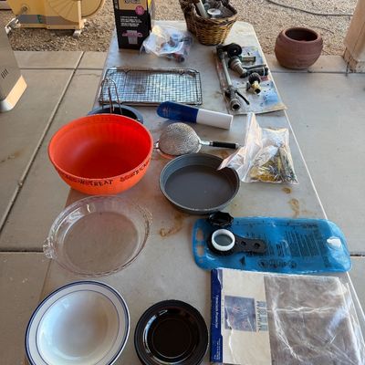 Sale Photo Thumbnail #246: Assorted household and outdoor items on a folding table, including kitchenware, a Halloween bowl, garden hose attachments, and a hydration bladder.