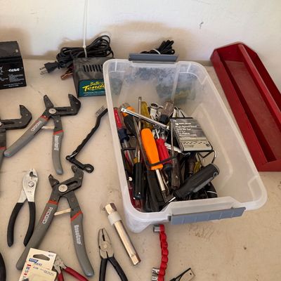 Assorted hand tools including Ridgid RoboGrip pliers, wire cutters, and a plastic bin filled with screwdrivers, drill bits, and other...